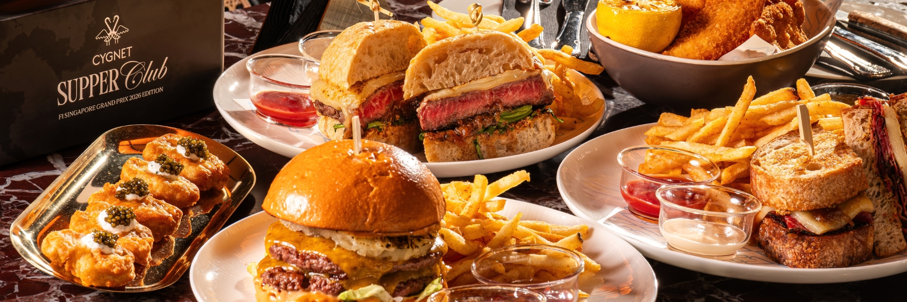 Burgers and steak sandwiches with fries, caviar-topped bites, dipping sauces, and a citrus drink fill the table.