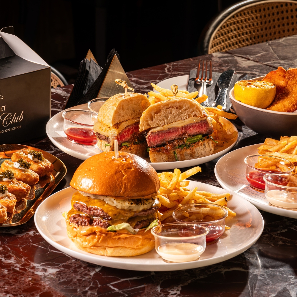Burgers, a sliced steak sandwich, fries, fried bites, and dipping sauces arranged on plates across a marble table.
