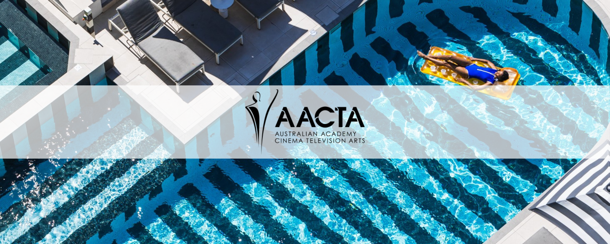 Aerial view of a pool with striped patterns, sun loungers alongside, and a person floating on a raft.