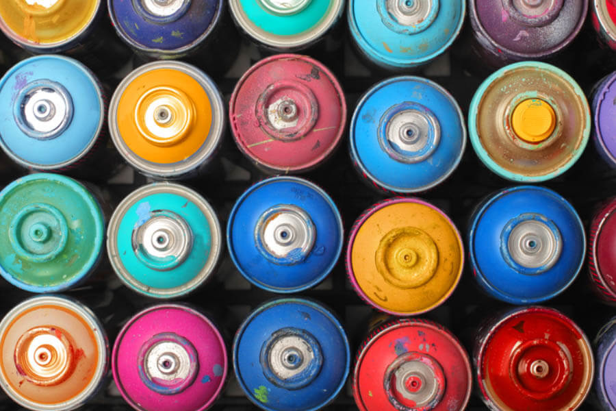 Top view of a collection of spray paint cans in various colors, displaying their caps and nozzles.