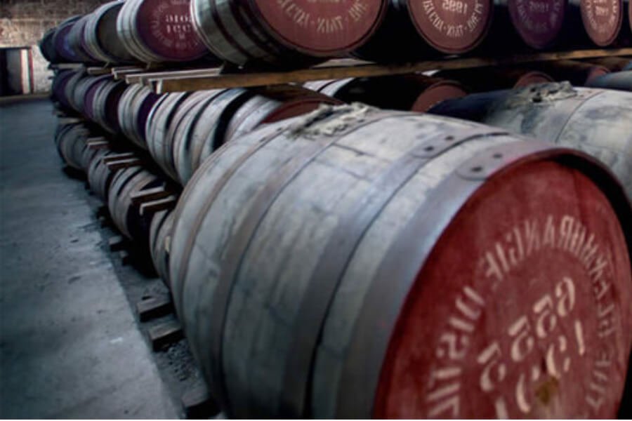 Rows of wooden barrels are stacked in a dimly lit cellar, with some displaying red markings on their ends.
