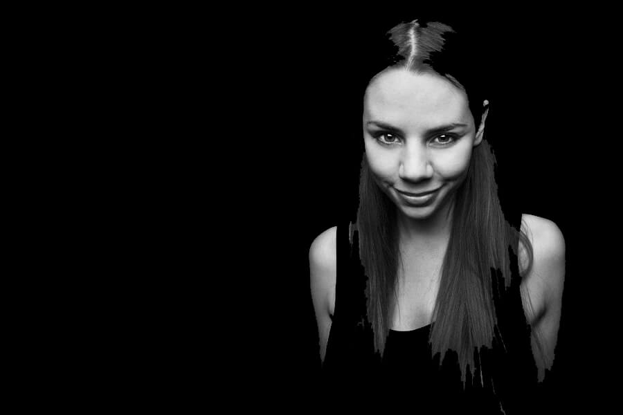 A woman with long dark hair smiles at the camera, set against a solid black background.