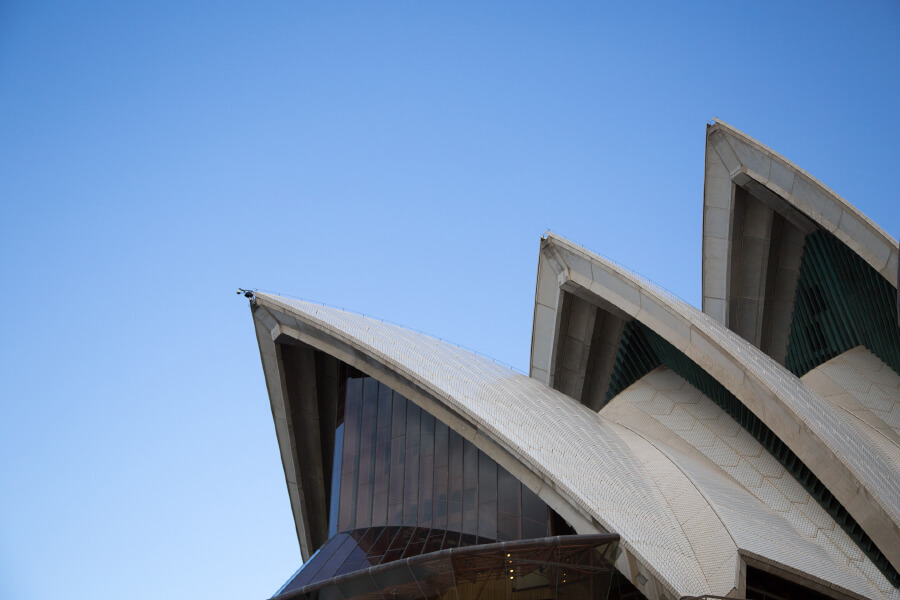 The upper sections of a modern architectural structure with distinctive, sail-like roofs against a clear blue sky.