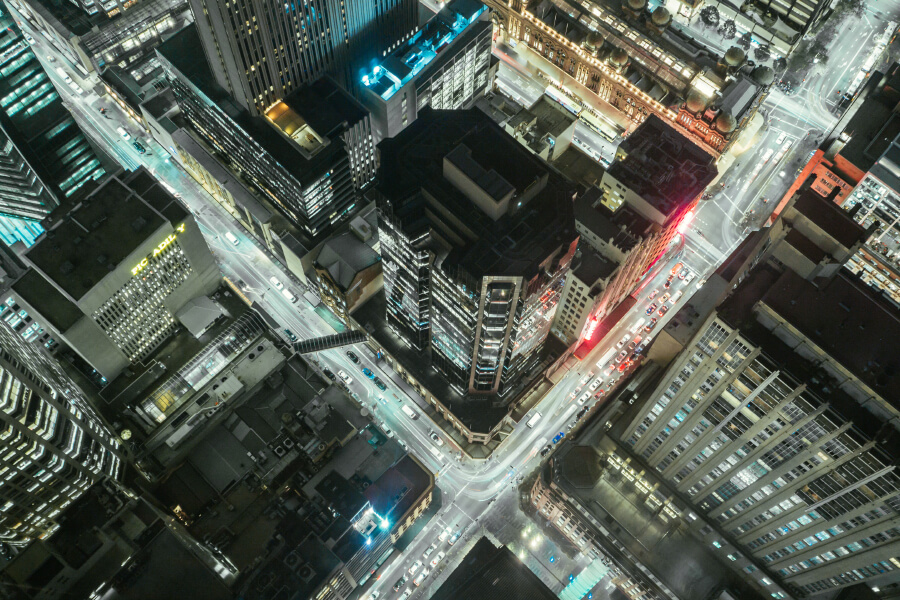 Aerial view of a city intersection at night, featuring illuminated buildings and busy traffic.