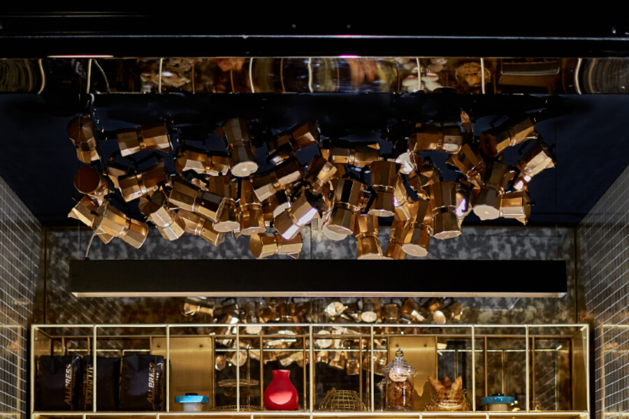A collection of gold and silver kitchenware hangs from the ceiling, with a display of colorful items in glass shelves below.