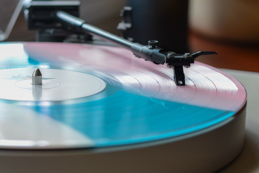 A close-up of a vinyl record player with a colorful pink and blue vinyl spinning, displaying the needle.
