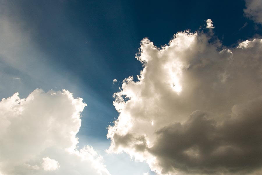 Fluffy white clouds against a blue sky with rays of light emerging from behind them.