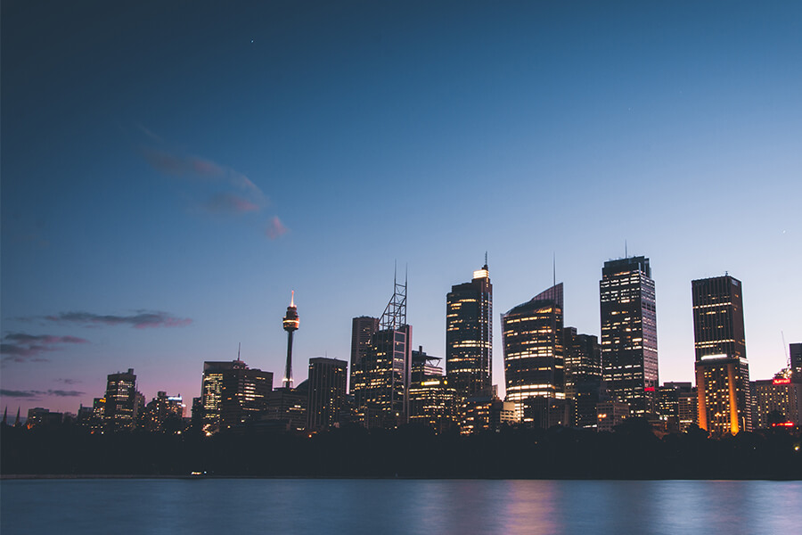 City skyline at dusk, featuring tall buildings and a clear sky transitioning from blue to purple.