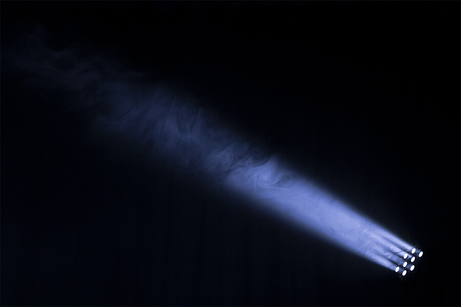 A strong beam of blue light emerges from multiple light sources, illuminating wisps of smoke against a dark background.