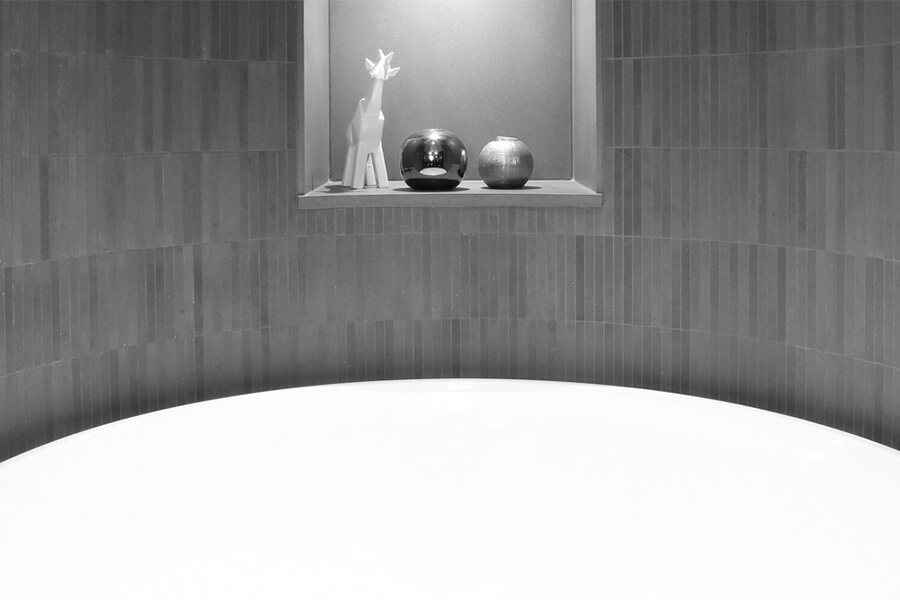 A modern bathroom scene featuring a curved white bathtub with a minimalist shelf displaying ceramic objects and a flower.