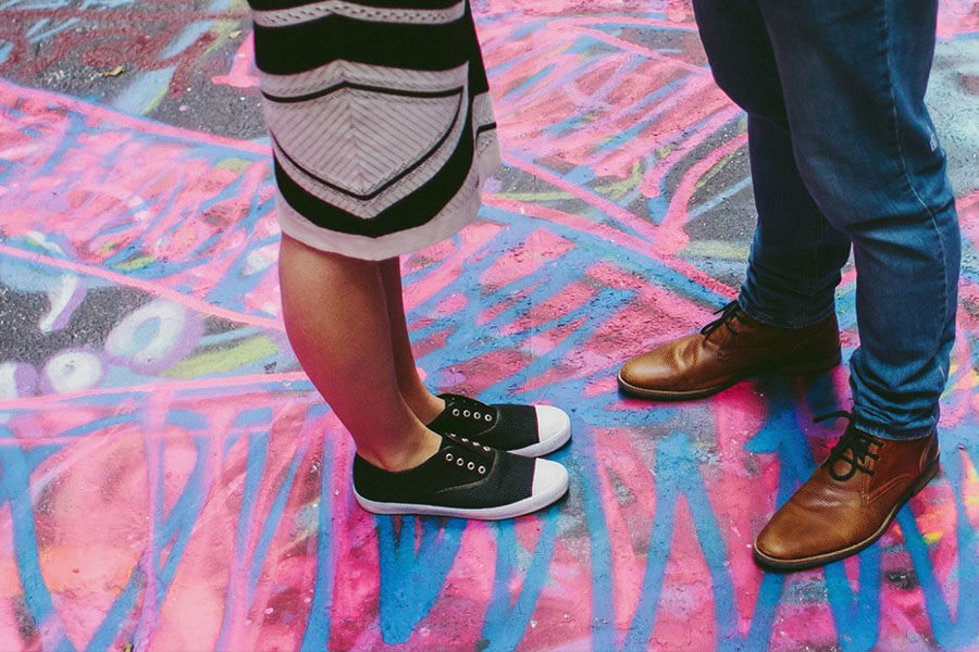 A close-up of two pairs of feet standing on a vibrant, graffiti-covered surface with pink and blue patterns.