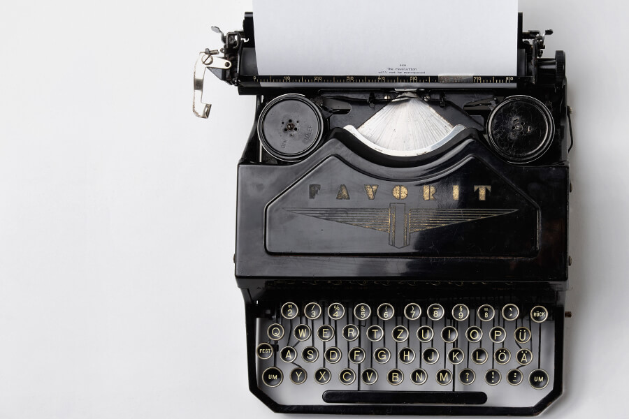 A vintage typewriter with a blank sheet of paper, featuring rounded keys and a decorative logo on its front.