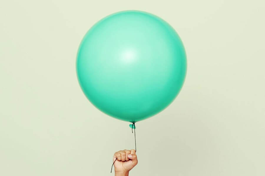 A hand holds a large turquoise balloon against a light beige background.