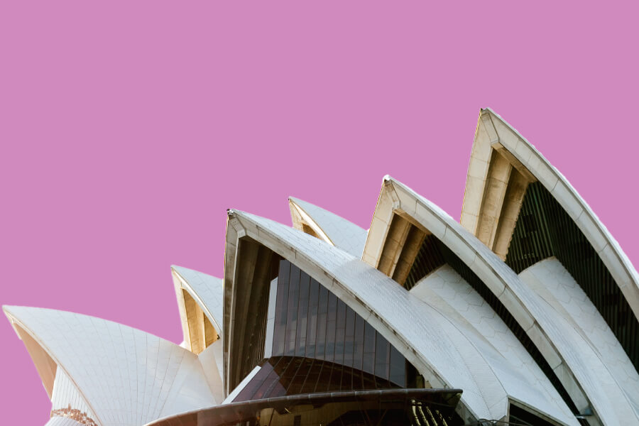 The angular, white structure of a modern building with sail-like rooftops is set against a pink background.