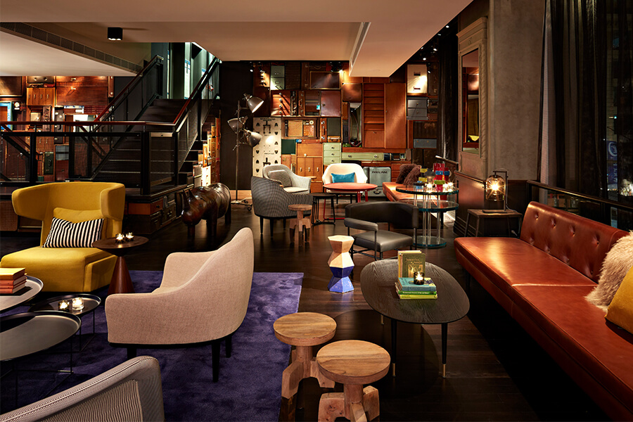 A stylish lounge with various seating options, colorful furniture, and a textured wall of cabinets in a warm, inviting atmosphere.