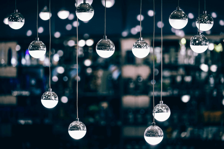 Hanging decorative light fixtures with clear round shapes, illuminated against a blurred background of varying colors.