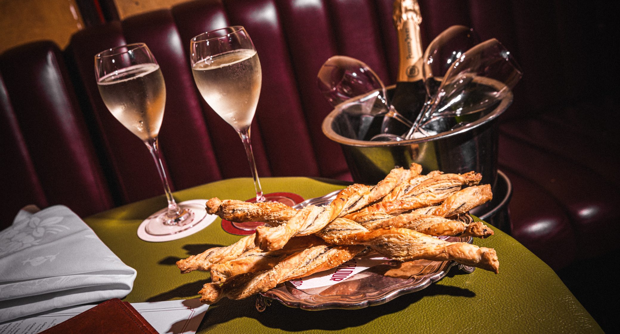 Perrier Jouët Champagne with two glasses and truffle parmesan twists on a green table at Parlour.