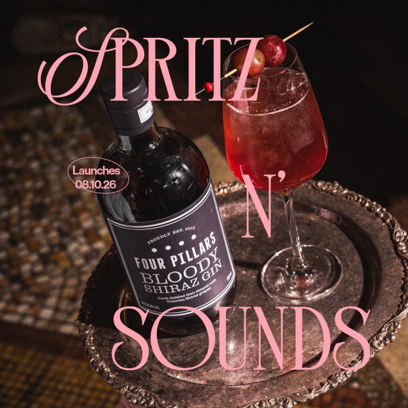 A bottle of Four Pillars Bloody Shiraz Gin beside a glass of red drink garnished with cherries, placed on a silver tray.