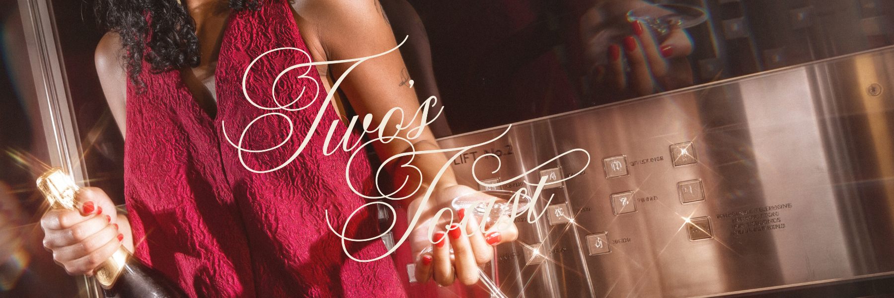 Cropped woman in a red dress holds a champagne bottle and glass beside elevator buttons, beneath large white cursive lettering.