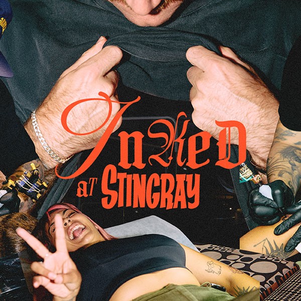 A close-up of hands pulling up a shirt, with a woman lying underneath, smiling and displaying a peace sign. Text overlay reads "Inked at Stingray."