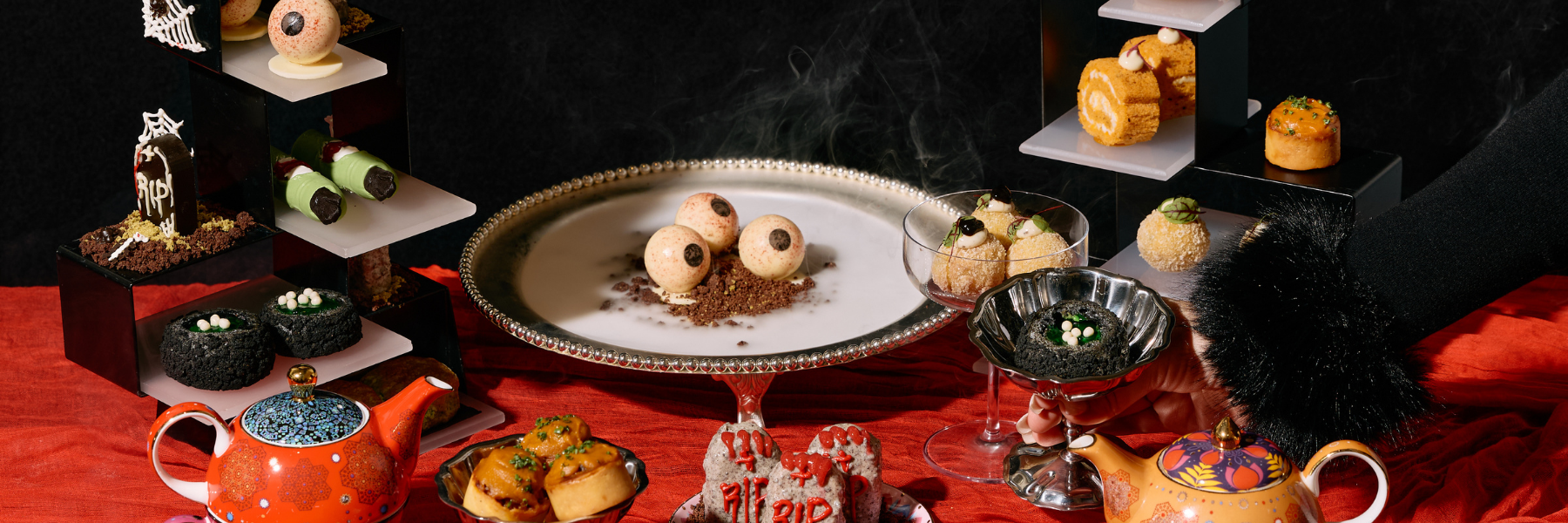 A colorful assortment of creatively designed desserts is displayed on tiered stands and plates, with a decorative teapot nearby.